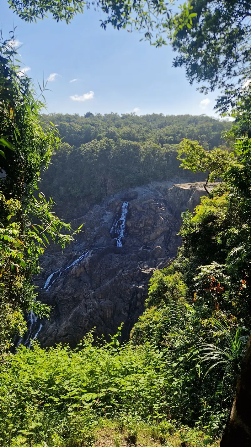 Barron Falls running in thin streams down a wide rock face, framed by rainforest under a blue sky