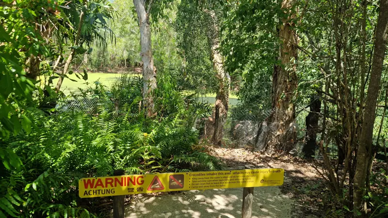 A yellow crocodile warning sign in front of a fenced lagoon