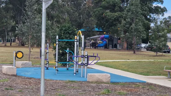 A colourful climbing frame on blue softfall beside a basketball hoop, with a fenced playground and spiral slide behind