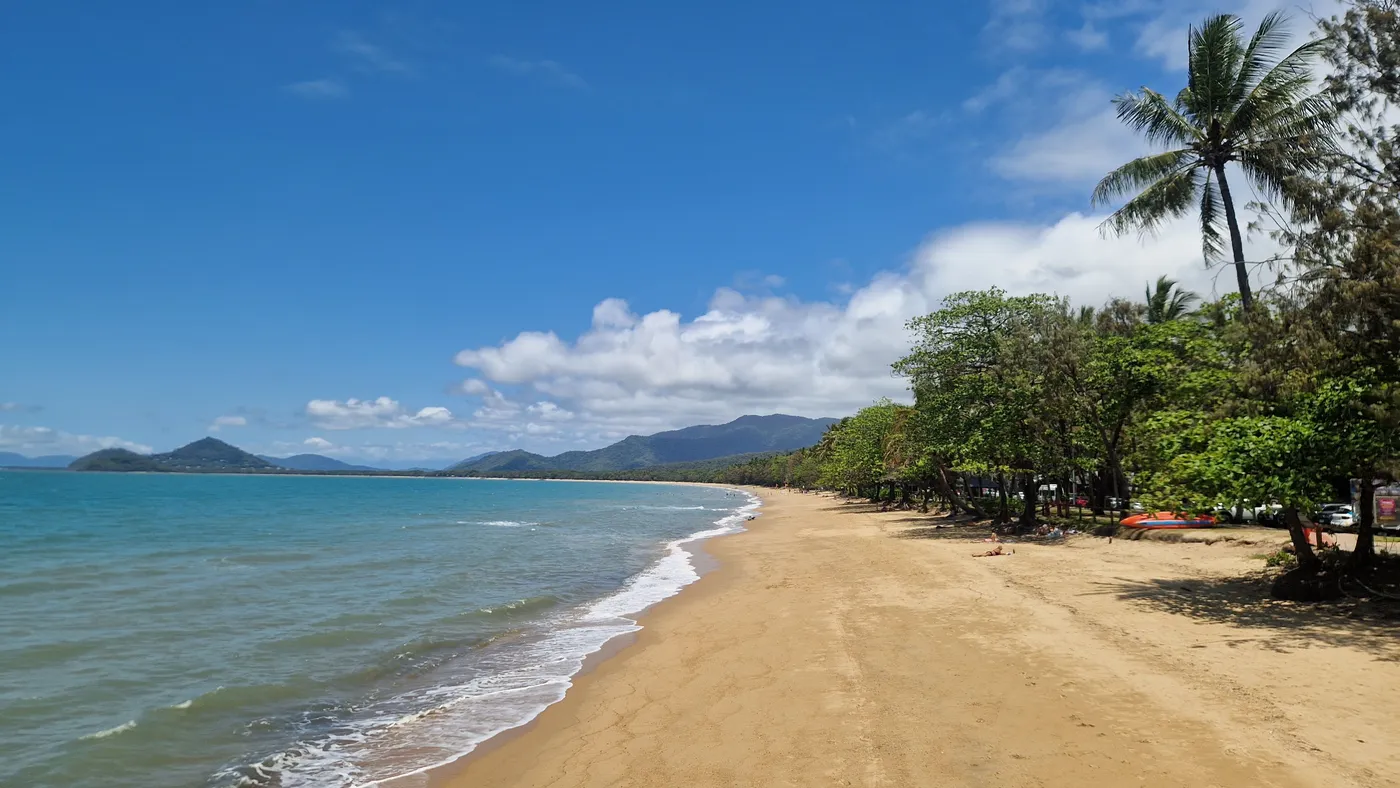 A long sandy beach curving away under palm trees, with green ranges behind