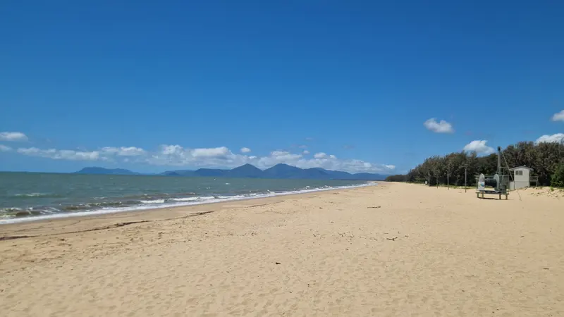 A long sandy beach with the ranges beyond and the stinger-net winch on the sand